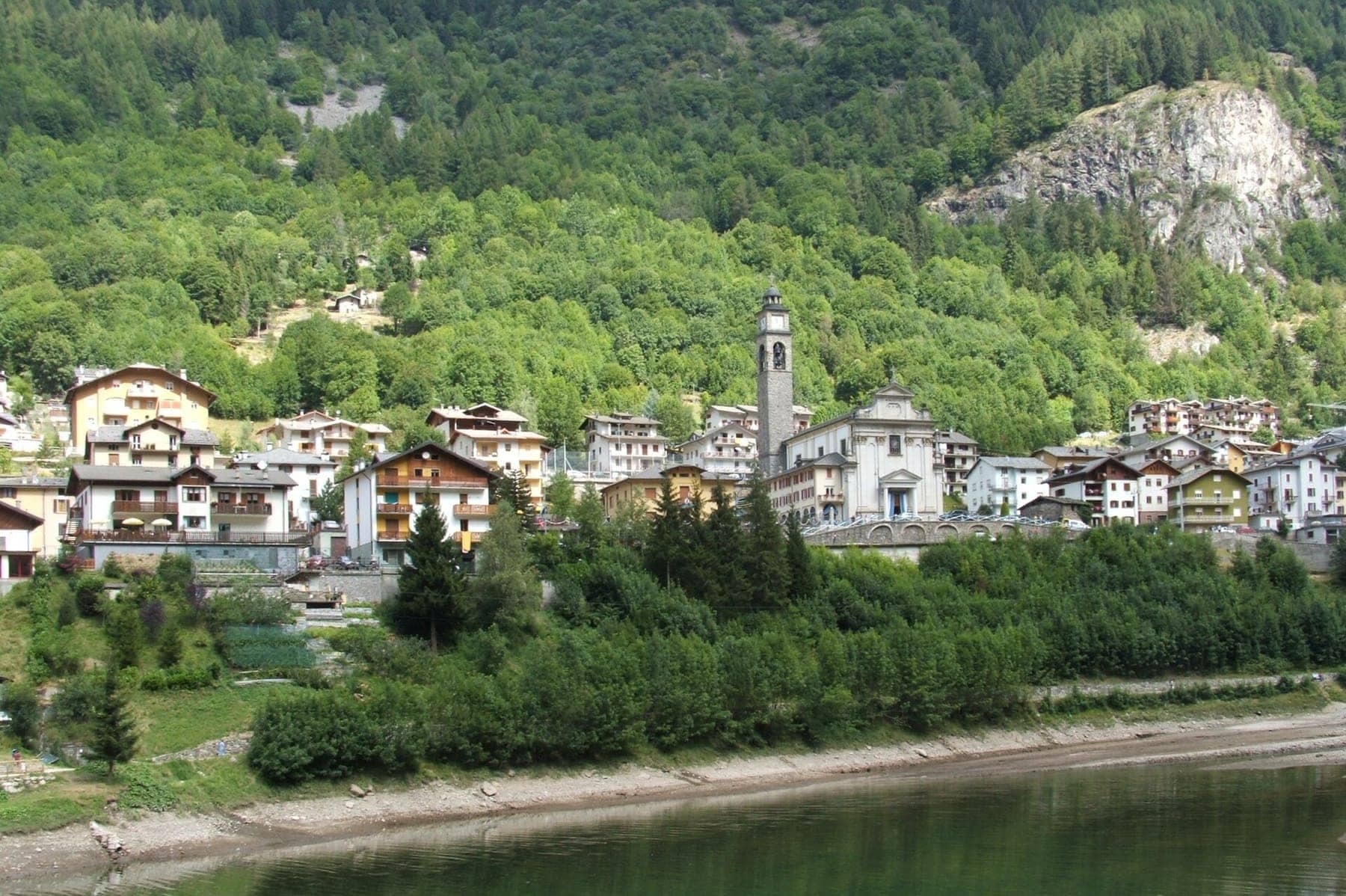 Il paese di Carona con il campanile e le case affacciate sul lago, tra i boschi dell'alta Valle Brembana