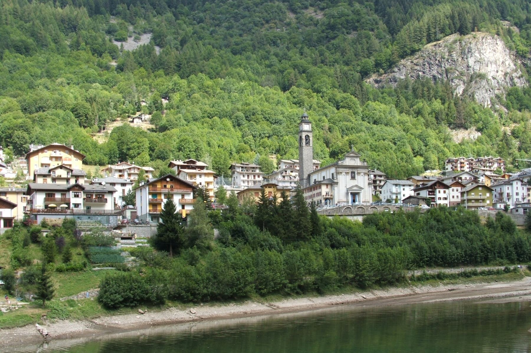 Il paese di Carona con il campanile e le case affacciate sul lago, tra i boschi dell'alta Valle Brembana