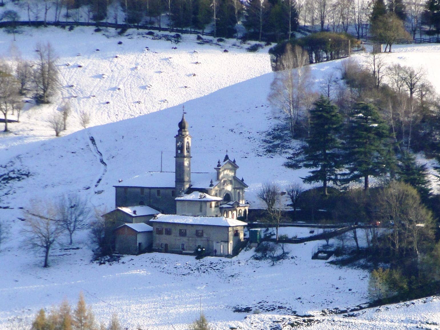 Il santuario della Madonna d'Erbia a Casnigo con il campanile a cipolla tra i prati innevati