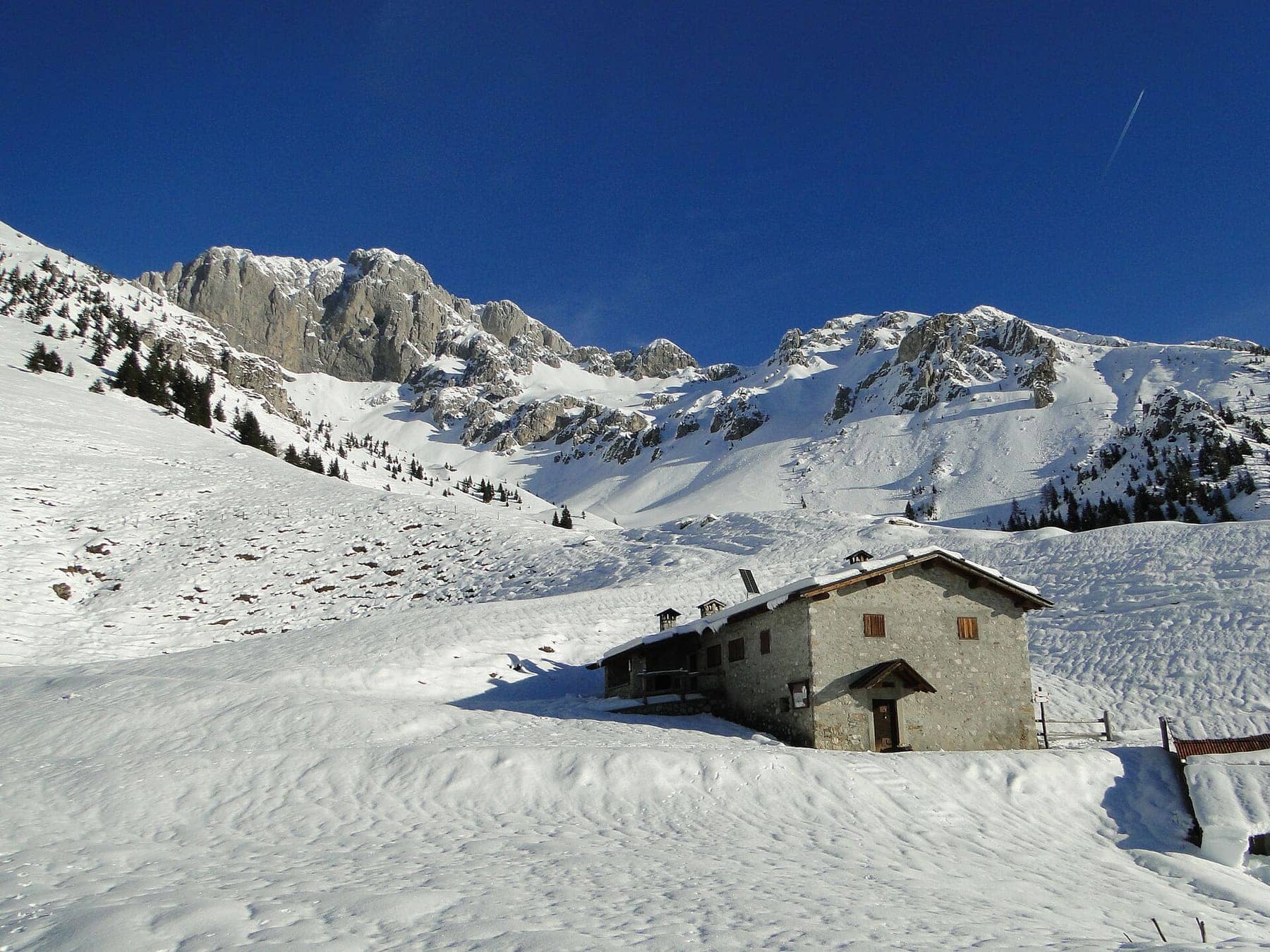 La Malga Presolana sotto la neve con le pareti del gruppo della Presolana alle spalle, nel territorio di Castione