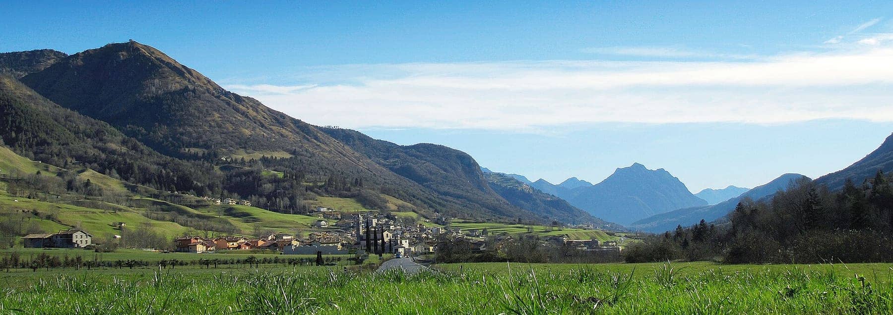 Cerete Basso con il campanile della parrocchiale tra i prati verdi dell'altopiano, con le montagne della bergamasca sullo sfondo