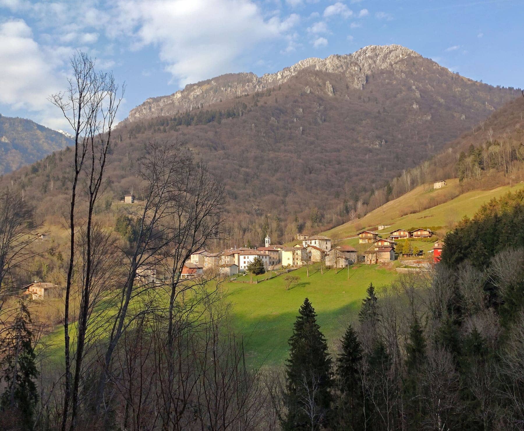 La contrada Tagliata di Costa Serina, con il campanile tra i prati sotto il versante boscoso e la cima rocciosa