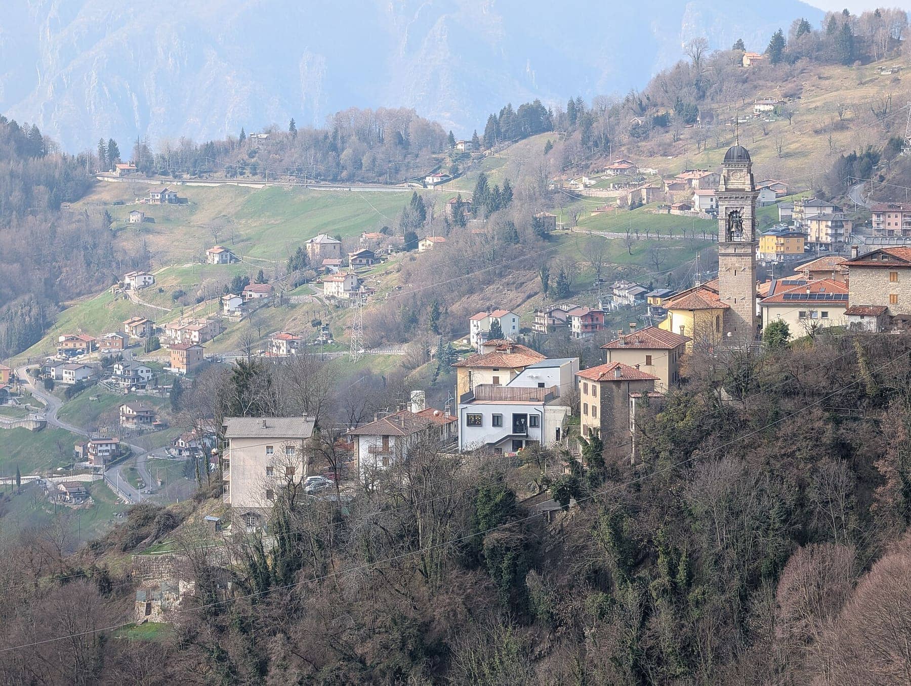 Dossena con il campanile della parrocchiale e le contrade sparse sui prati del versante, visti dal ponte tibetano