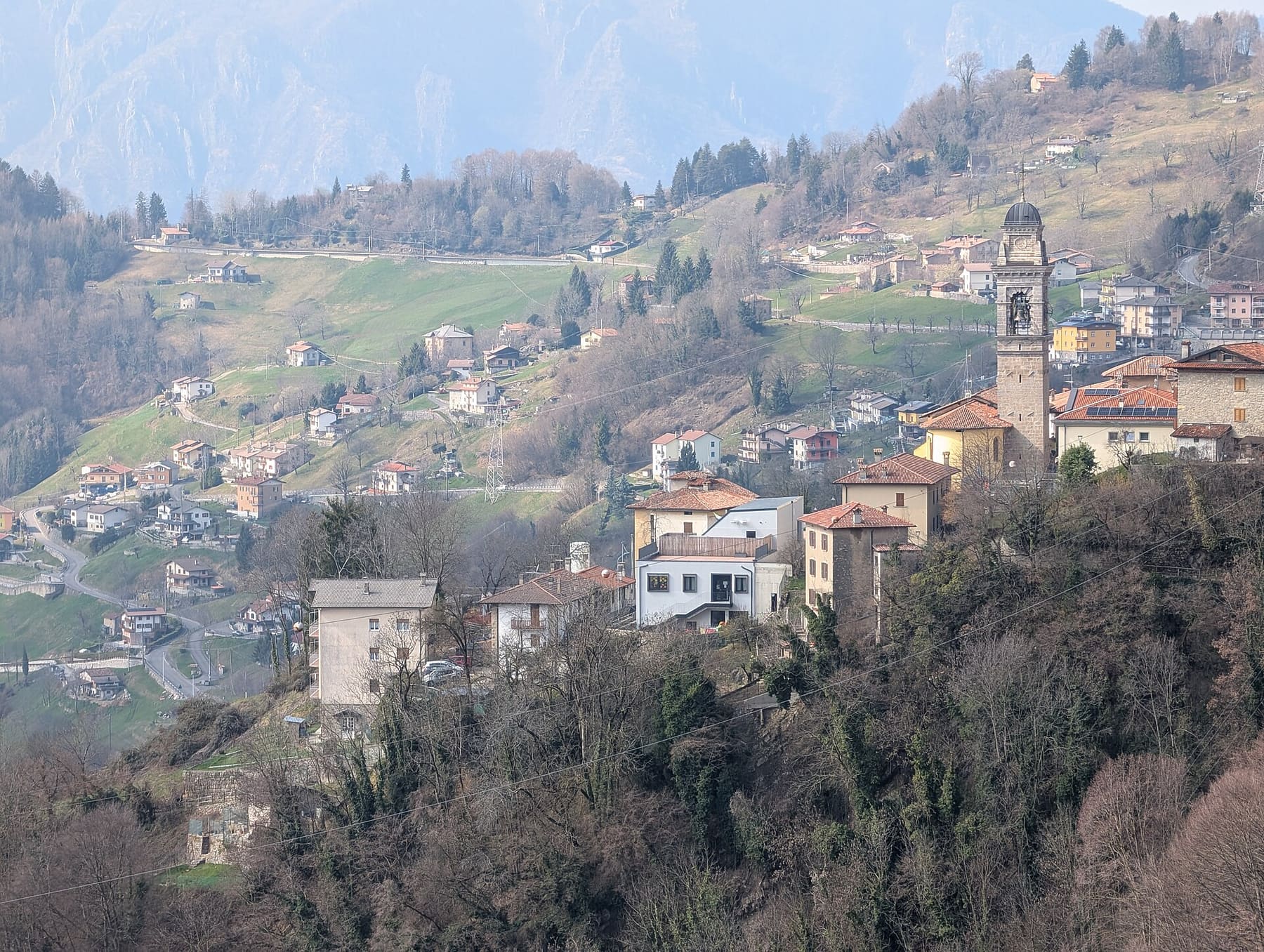 Dossena con il campanile della parrocchiale e le contrade sparse sui prati del versante, visti dal ponte tibetano