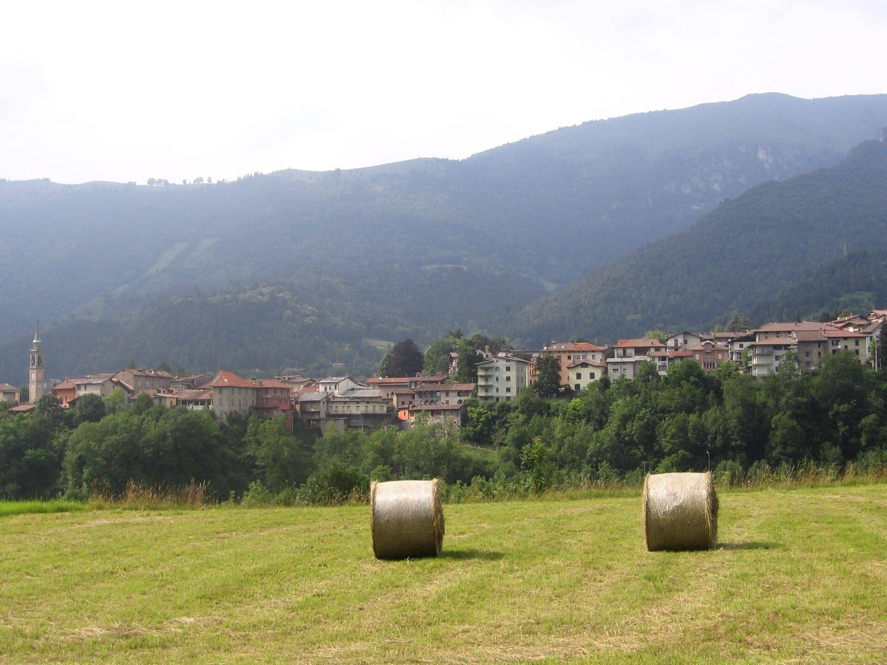 Fino del Monte visto dai prati con le rotoballe di fieno, il campanile e i boschi dell'altopiano di Clusone