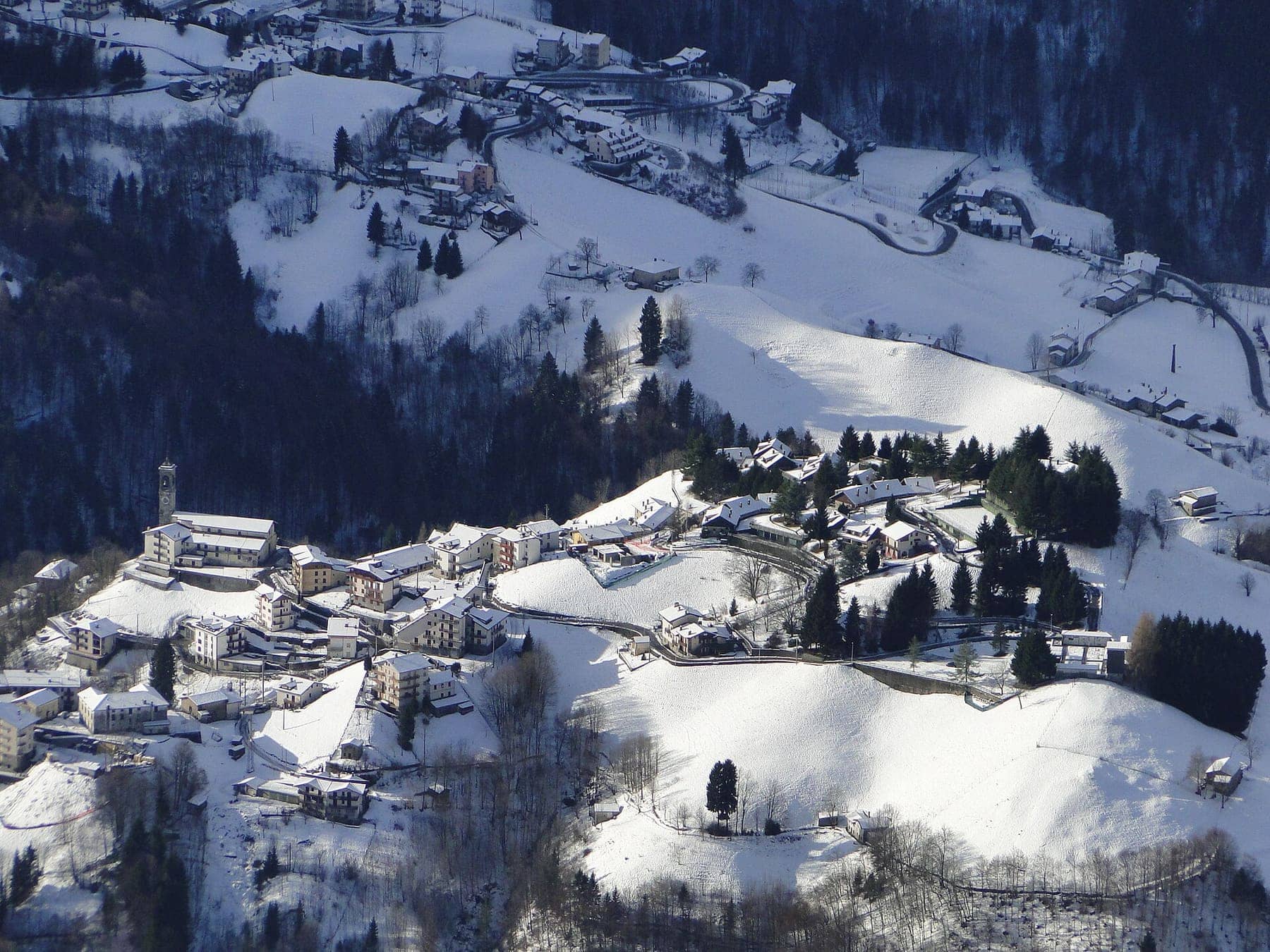 Zambla Bassa, frazione di Oltre il Colle, coperta di neve con la chiesa e i prati bianchi vista dalla cima del Grem