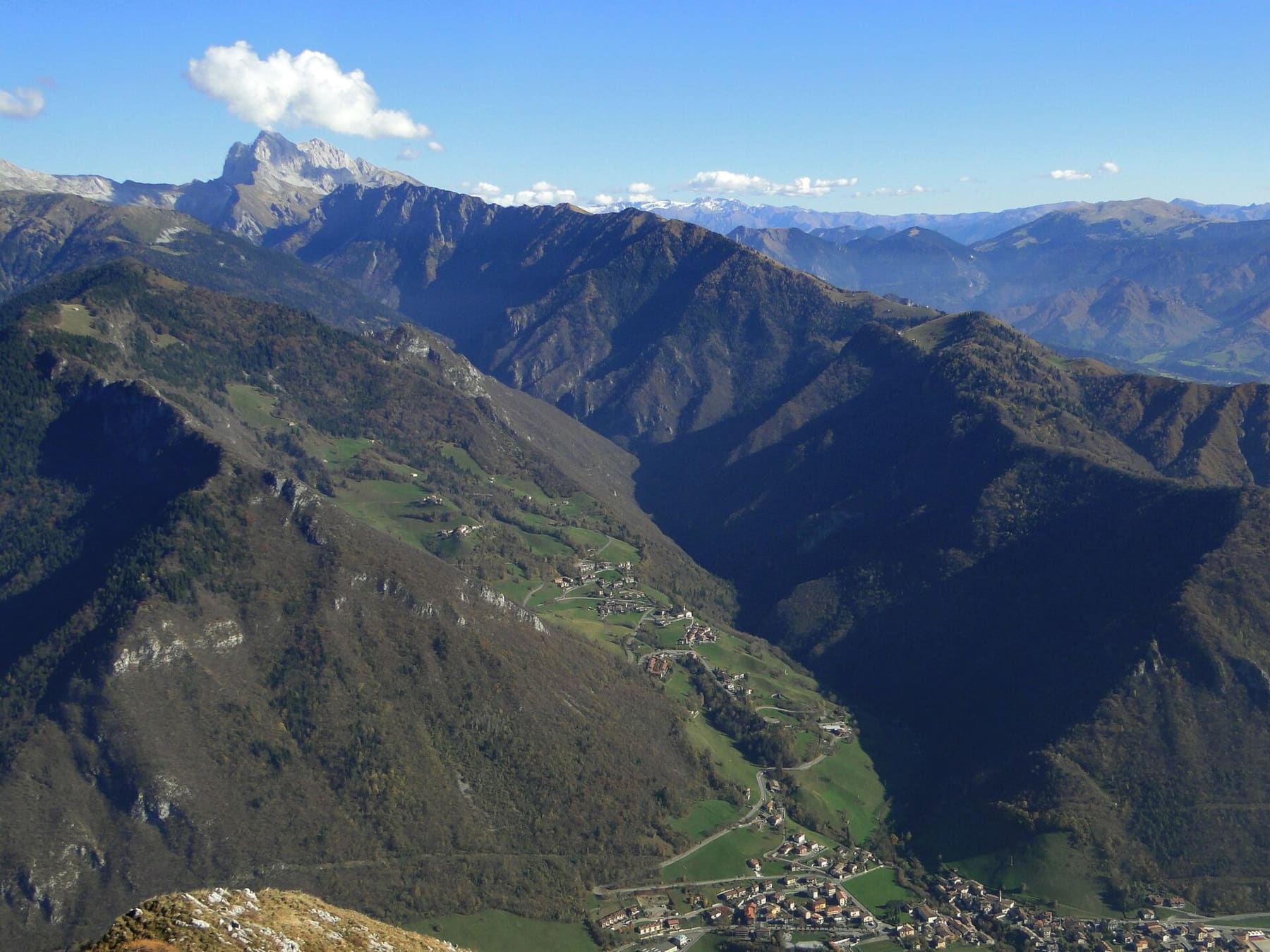 La Valzurio vista dall'alto in autunno, con i prati e le frazioni di Oltressenda Alta sul versante e le cime rocciose delle Orobie sullo sfondo