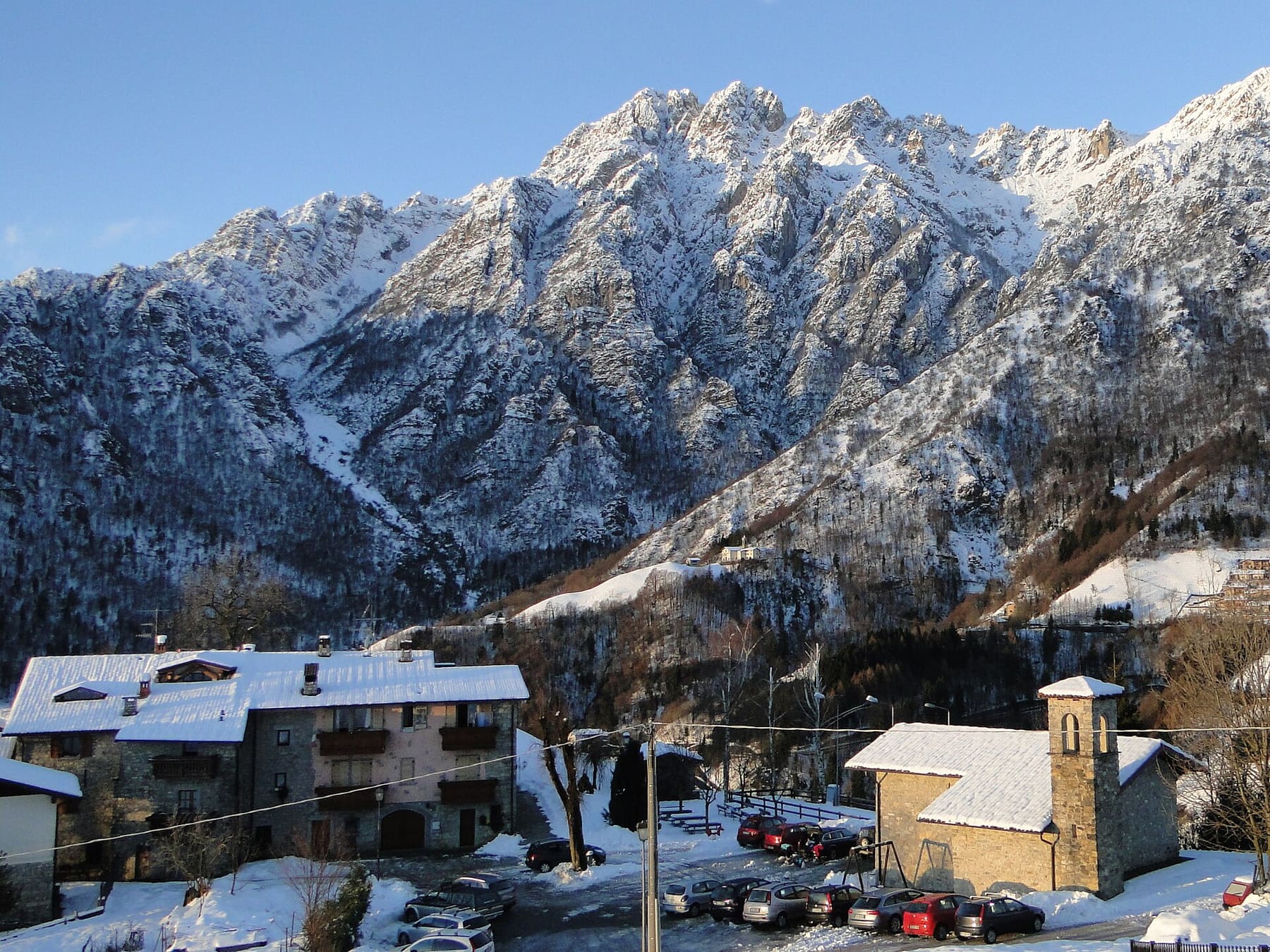 Case in pietra e chiesetta in località Plazza a Oneta, sotto le pareti rocciose innevate della Val del Riso