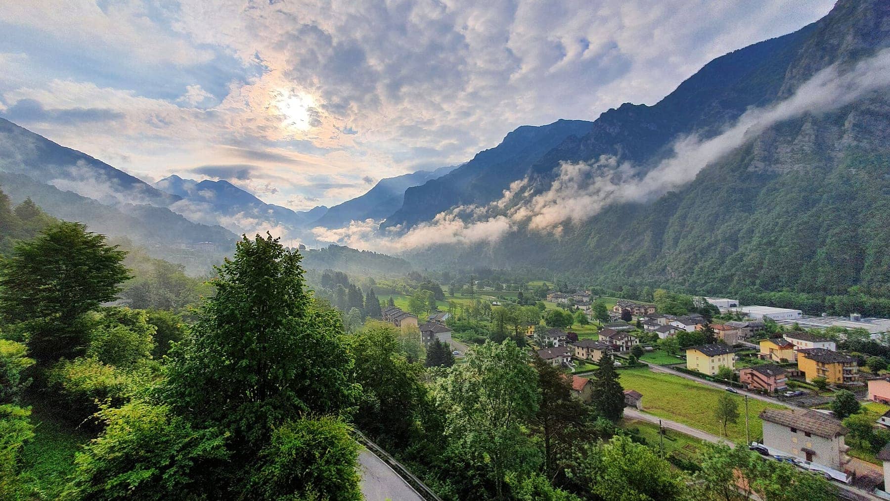 Le case di Piazza Brembana nel fondovalle dell'alta Valle Brembana al mattino, con nuvole basse tra i monti