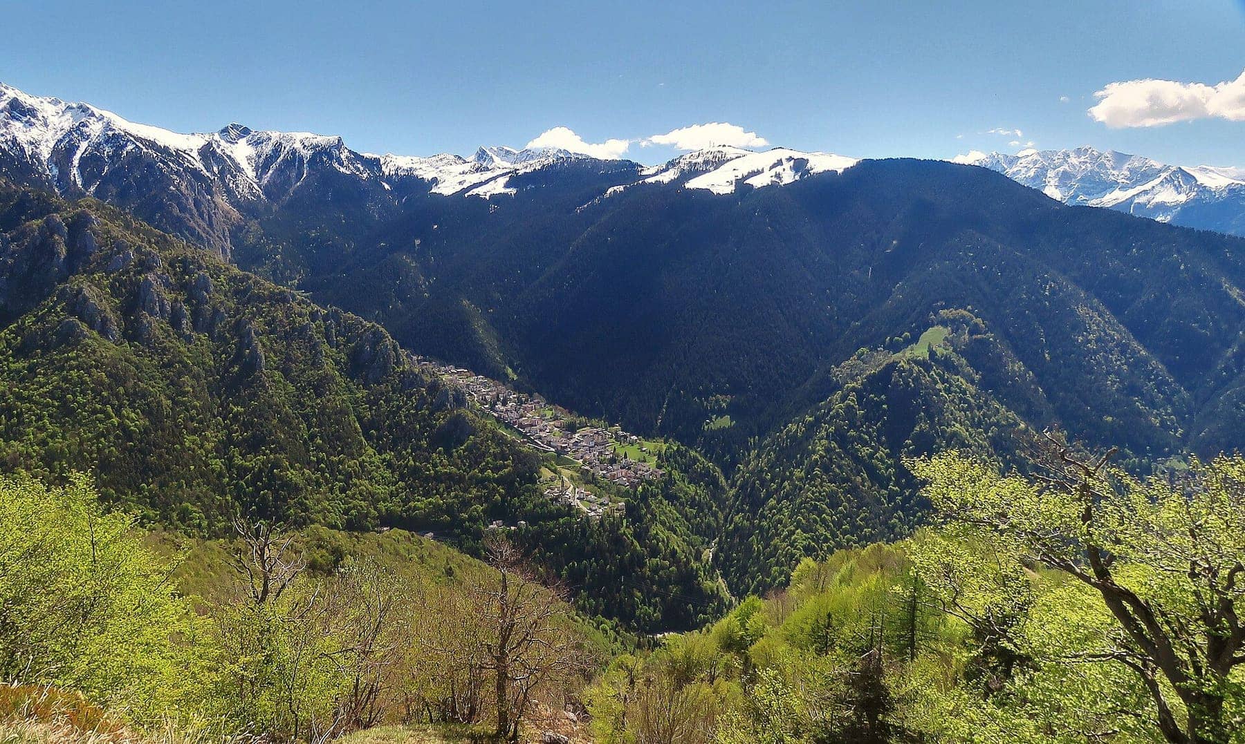 Piazzatorre in primavera nella conca boscosa ai piedi del Monte Torcola, con le cime innevate sullo sfondo
