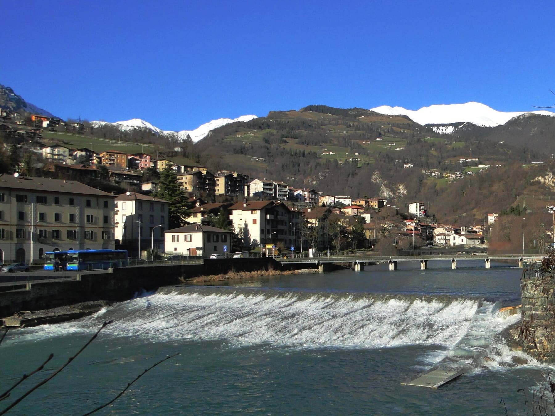 Il fiume Serio con la briglia a Ponte Nossa, il paese e le montagne innevate della Valle Seriana in una giornata limpida
