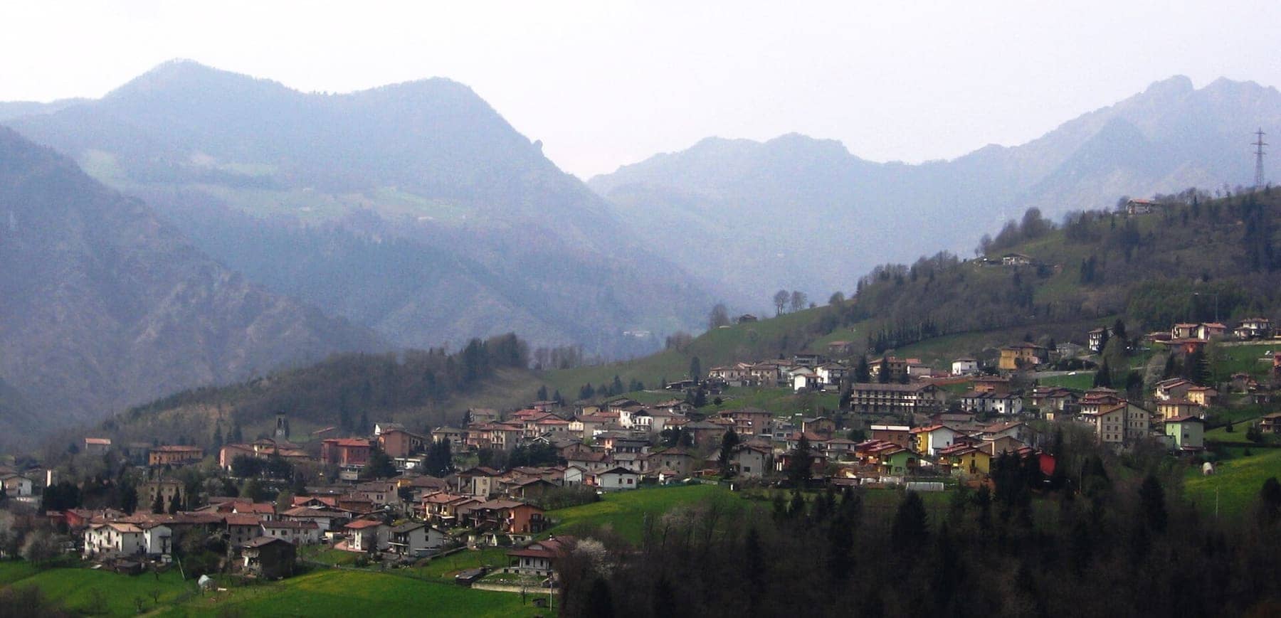 Il paese di Premolo adagiato sui prati del versante destro della media Valle Seriana, con le Prealpi bergamasche sullo sfondo