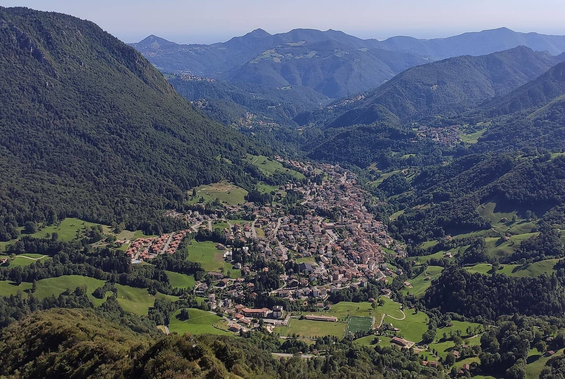 Serina e la conca della Val Serina viste dall'alto dal monte Castello, con prati e boschi d'estate