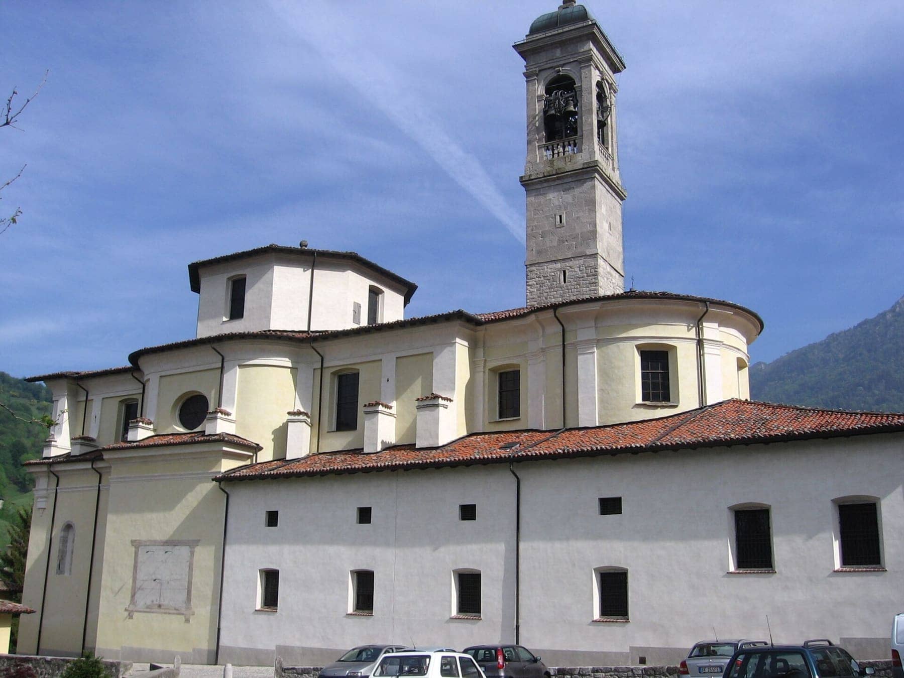 La chiesa parrocchiale di Santa Maria Annunciata a Serina, con il campanile in pietra e il tiburio, sotto un cielo azzurro