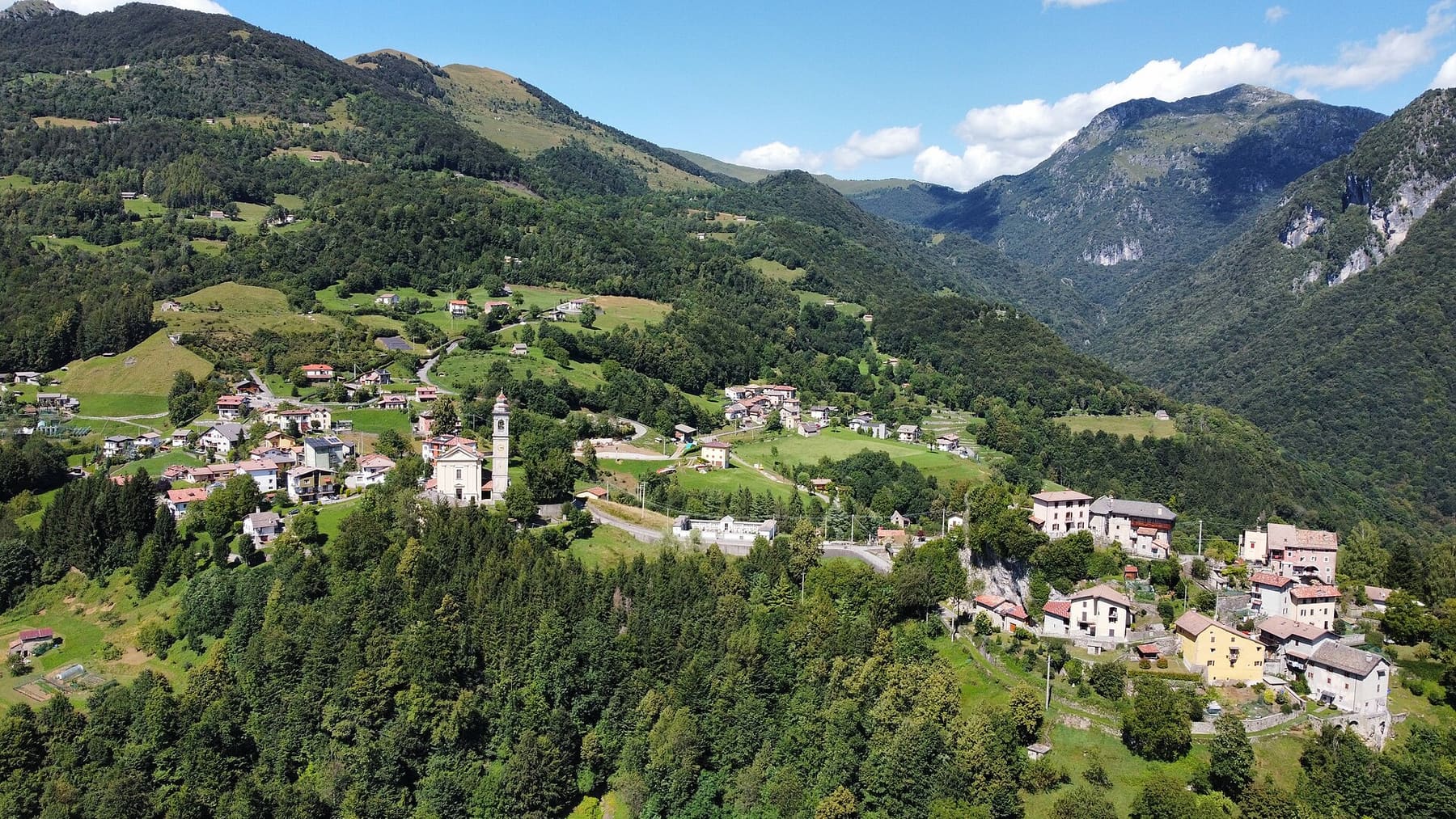 Veduta aerea di Pizzino, frazione di Taleggio, con la chiesa di Sant'Ambrogio tra prati e boschi