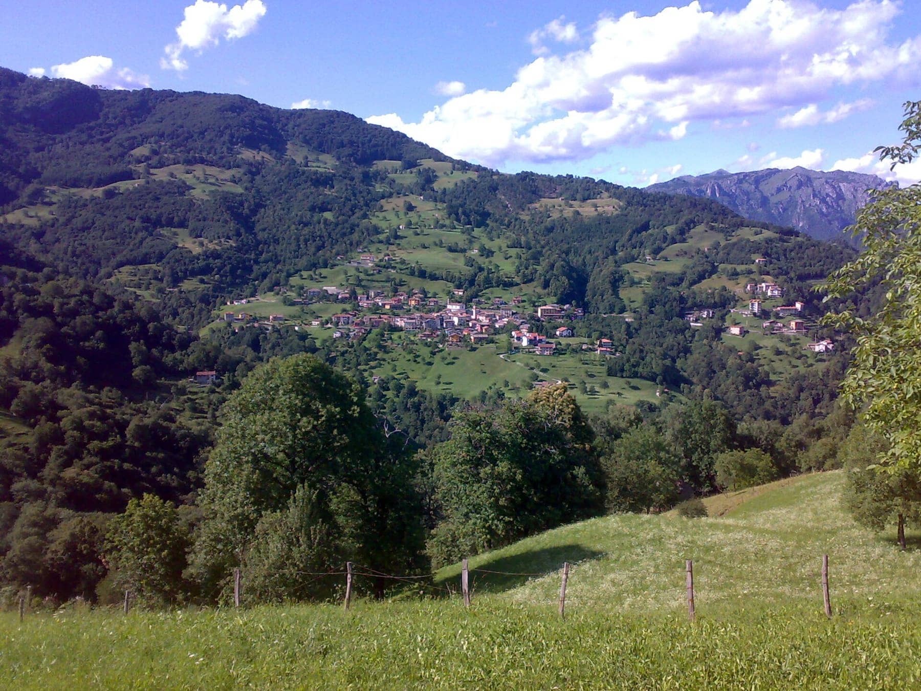 Gerosa, frazione di Val Brembilla, adagiata sul versante tra prati e boschi, con le cime rocciose sullo sfondo