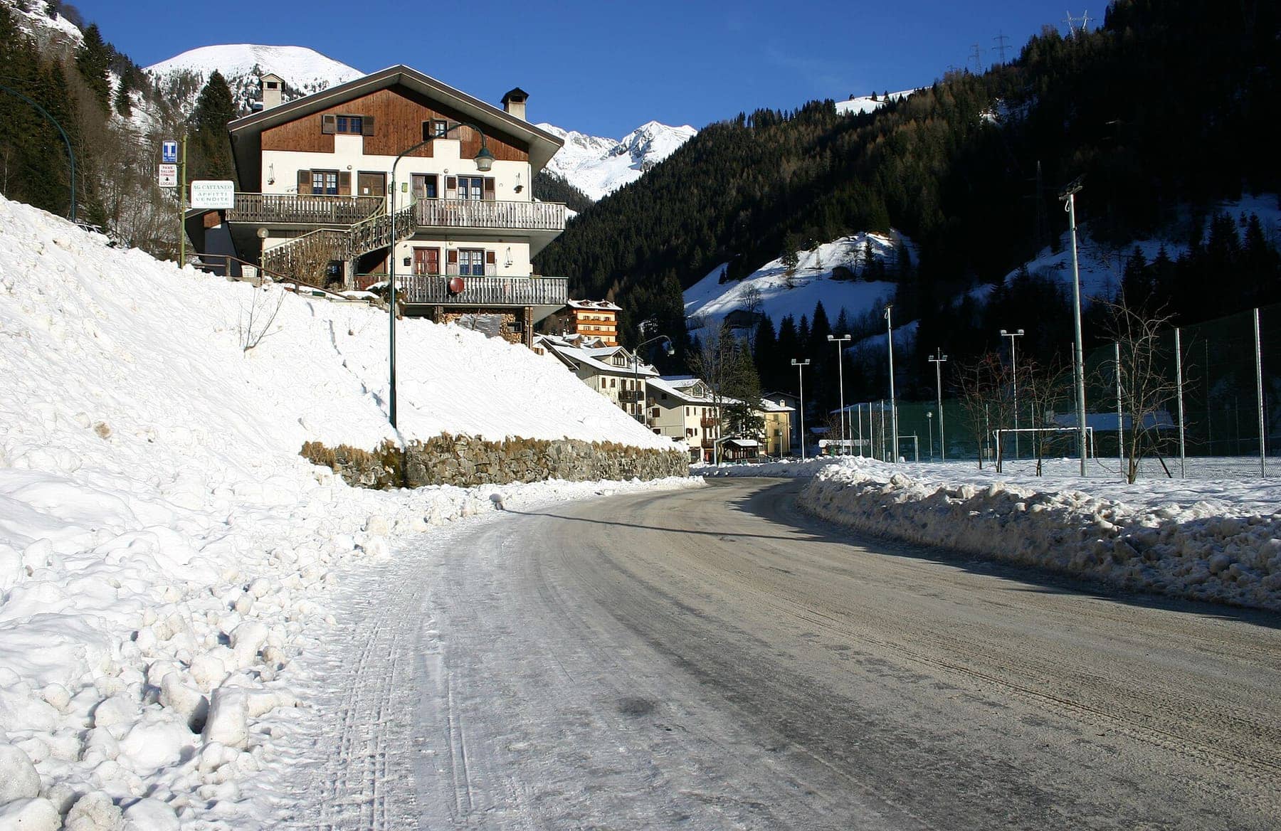 Le prime case di Valleve in inverno, con la strada innevata e le cime dell'Alta Valle Brembana al sole
