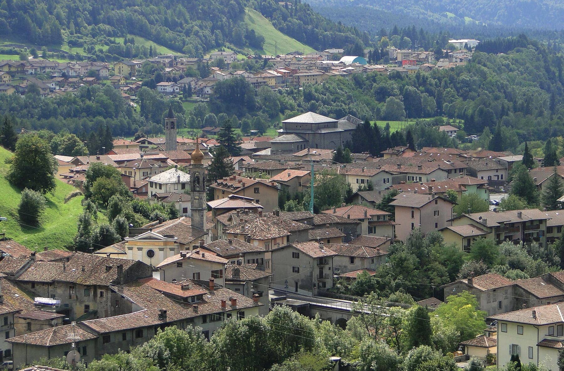 Il centro di Villa d'Ogna con i campanili e i tetti in pietra, tra i prati dell'alta Valle Seriana