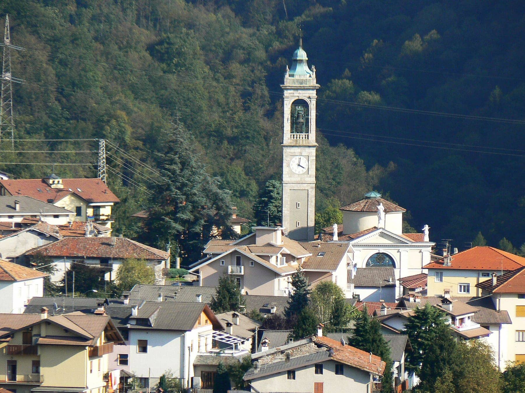 Il campanile e la chiesa di Santa Maria Assunta a Endenna, frazione di Zogno, tra i tetti del paese e il bosco