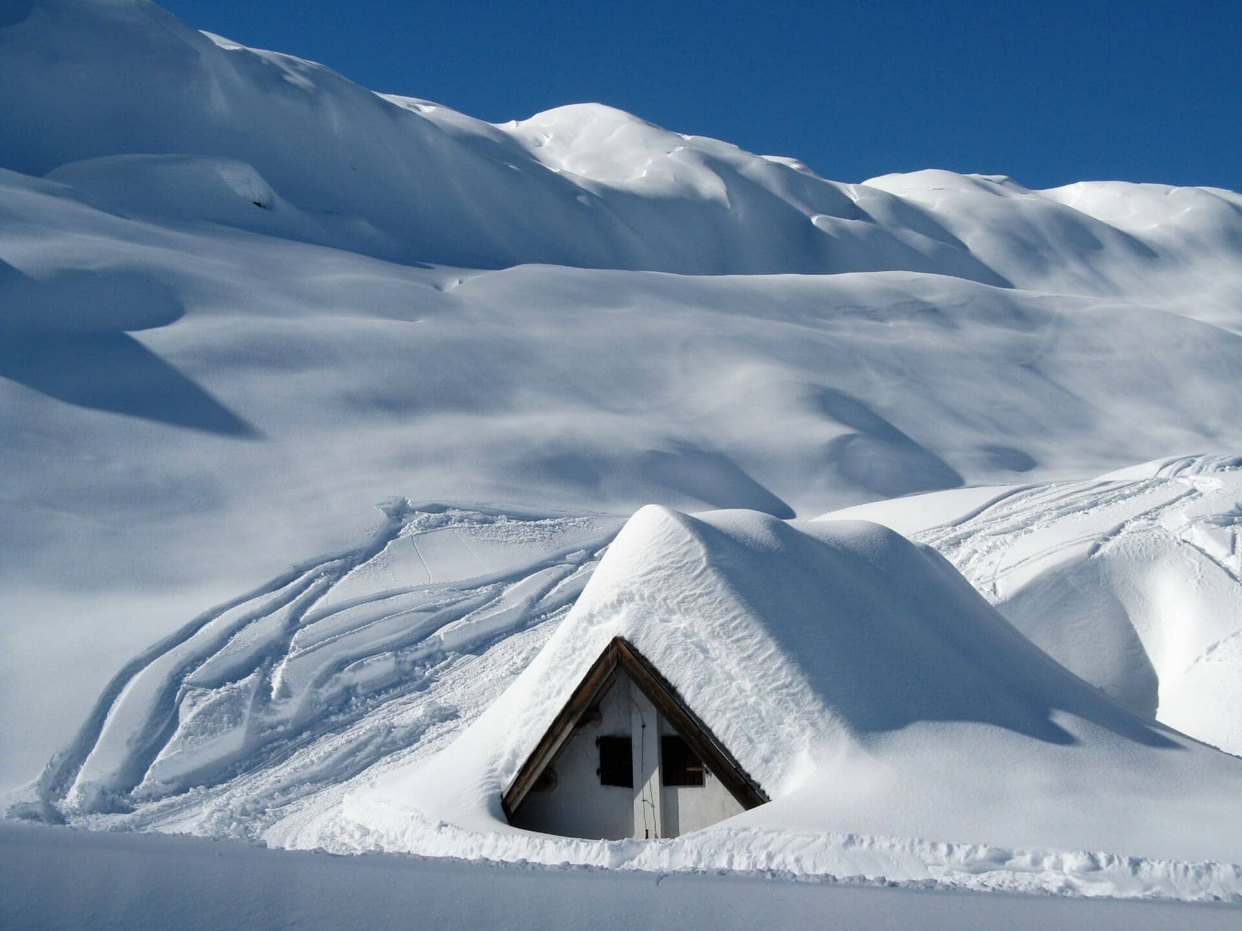 Baita sepolta dalla neve fresca nella conca del rifugio Albani sopra Colere, in Val di Scalve, sotto un cielo terso