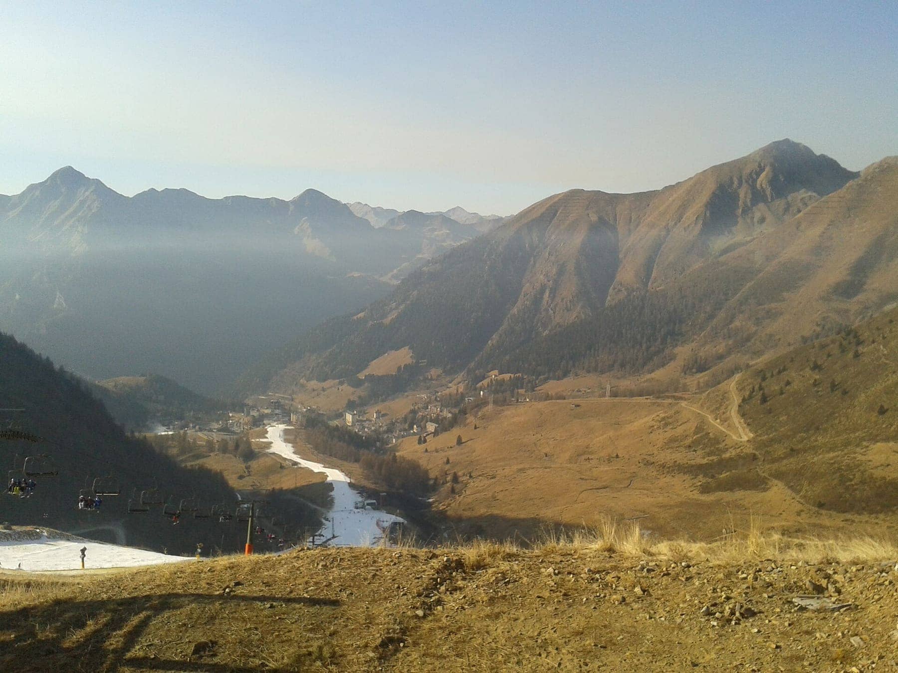 La pista di Foppolo con neve programmata a inizio stagione, la seggiovia e il paese in fondo alla conca, con i pendii ancora spogli