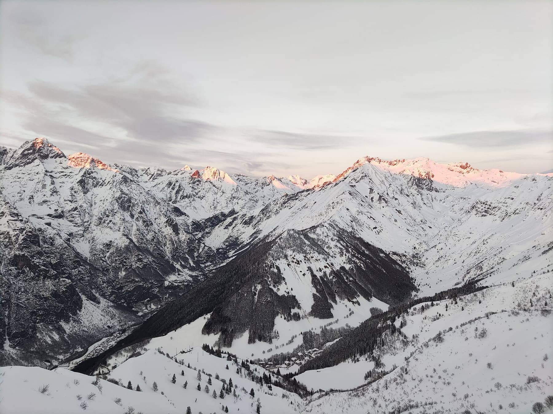 Le Orobie innevate al tramonto viste dai pendii sciistici sopra Lizzola, con le case sparse nel fondovalle