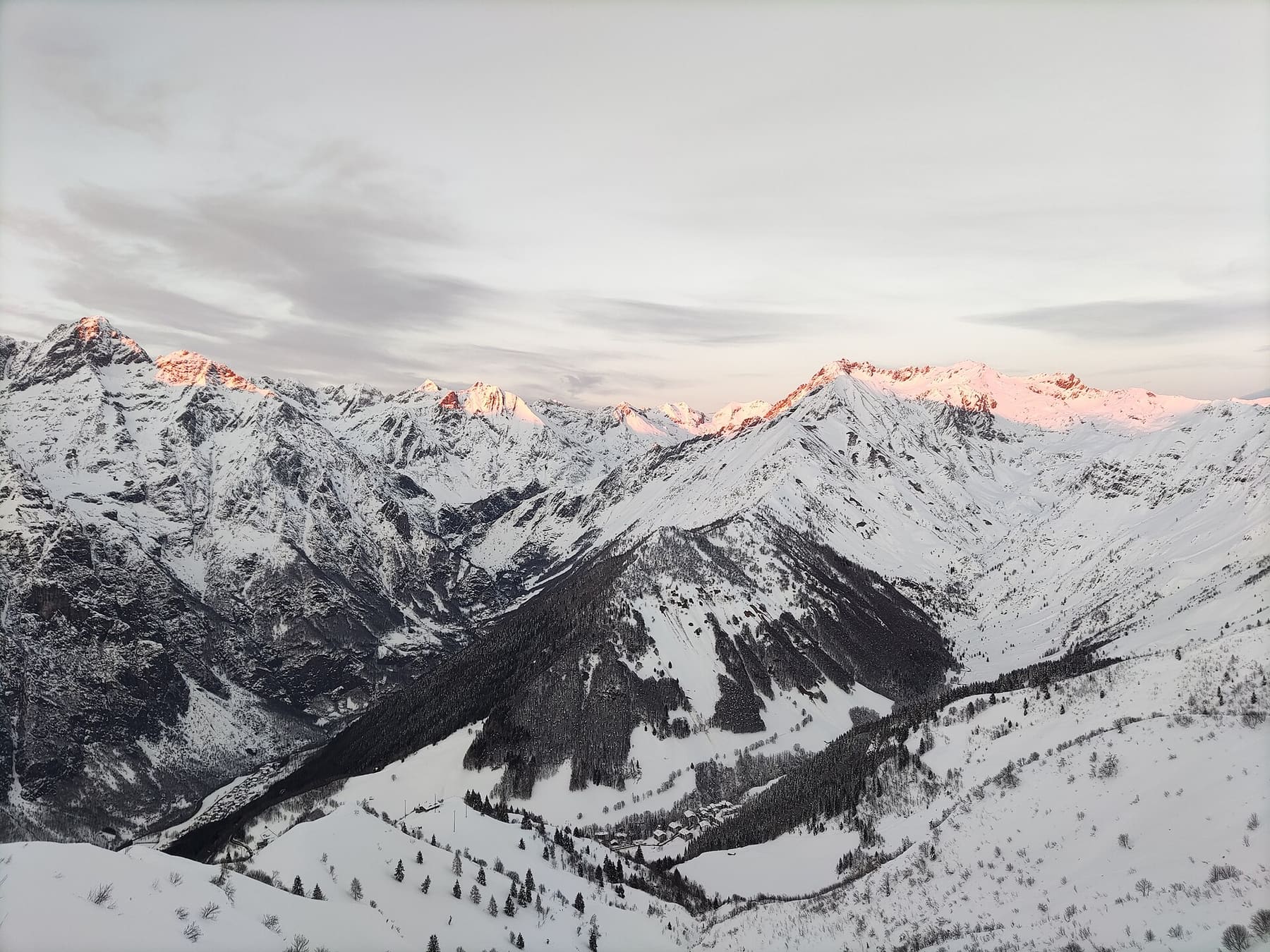 Le Orobie innevate al tramonto viste dai pendii sciistici sopra Lizzola, con le case sparse nel fondovalle
