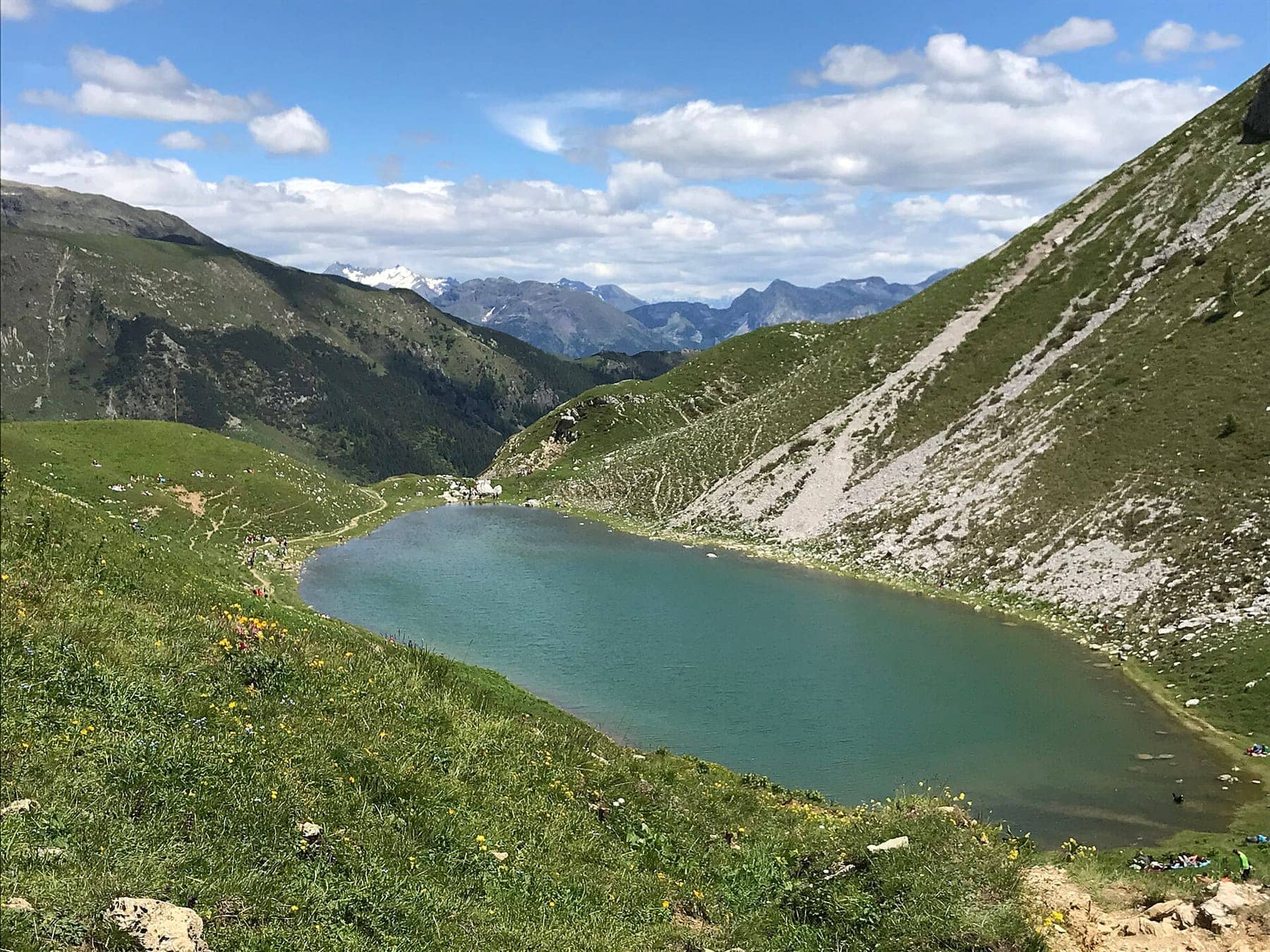 Il lago Branchino dal sentiero del passo, con l'acqua verde-azzurra tra i pascoli e le cime delle Orobie all'orizzonte