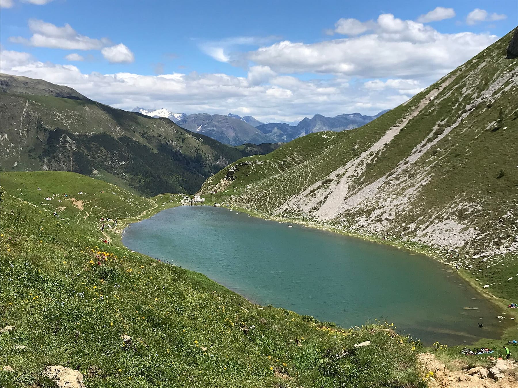 Il lago Branchino dal sentiero del passo, con l'acqua verde-azzurra tra i pascoli e le cime delle Orobie all'orizzonte