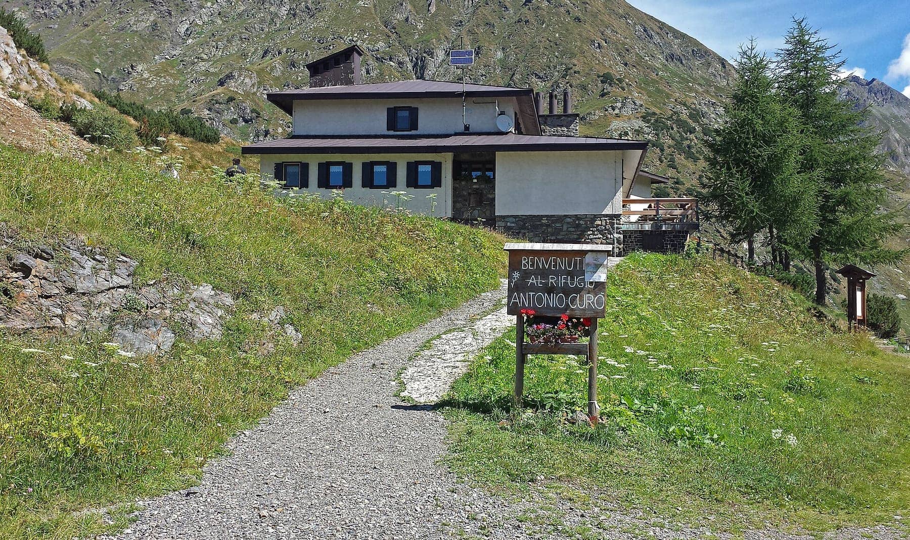 Il sentiero d'arrivo al rifugio Antonio Curò sopra Valbondione, con il cartello di benvenuto e l'edificio del rifugio