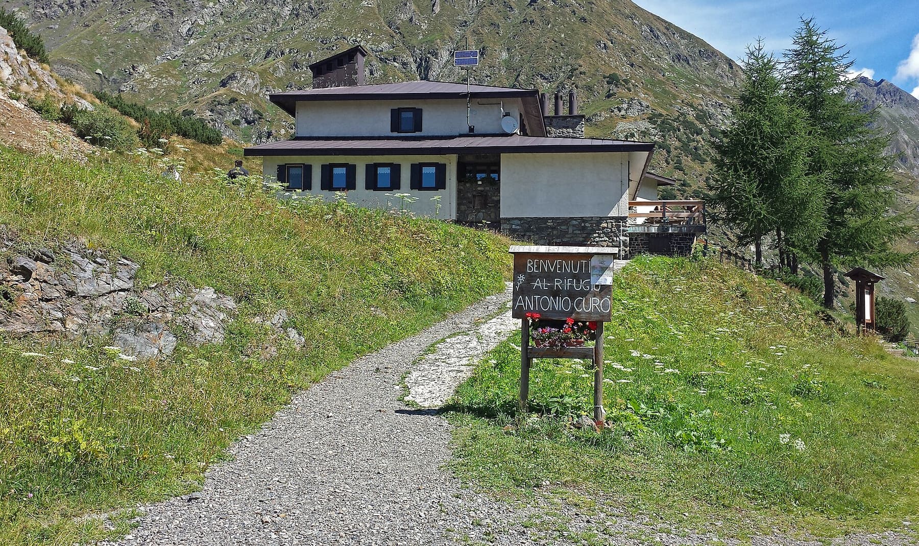 Il sentiero d'arrivo al rifugio Antonio Curò sopra Valbondione, con il cartello di benvenuto e l'edificio del rifugio