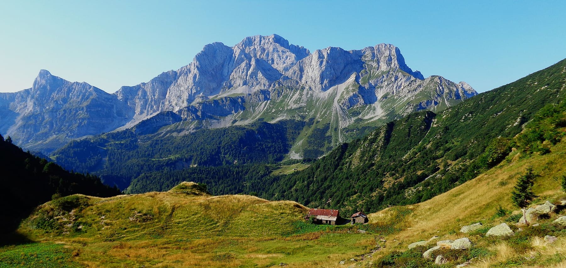 Il pizzo Arera visto dal sentiero che sale ai Laghi Gemelli, con una baita tra i pascoli e il cielo terso