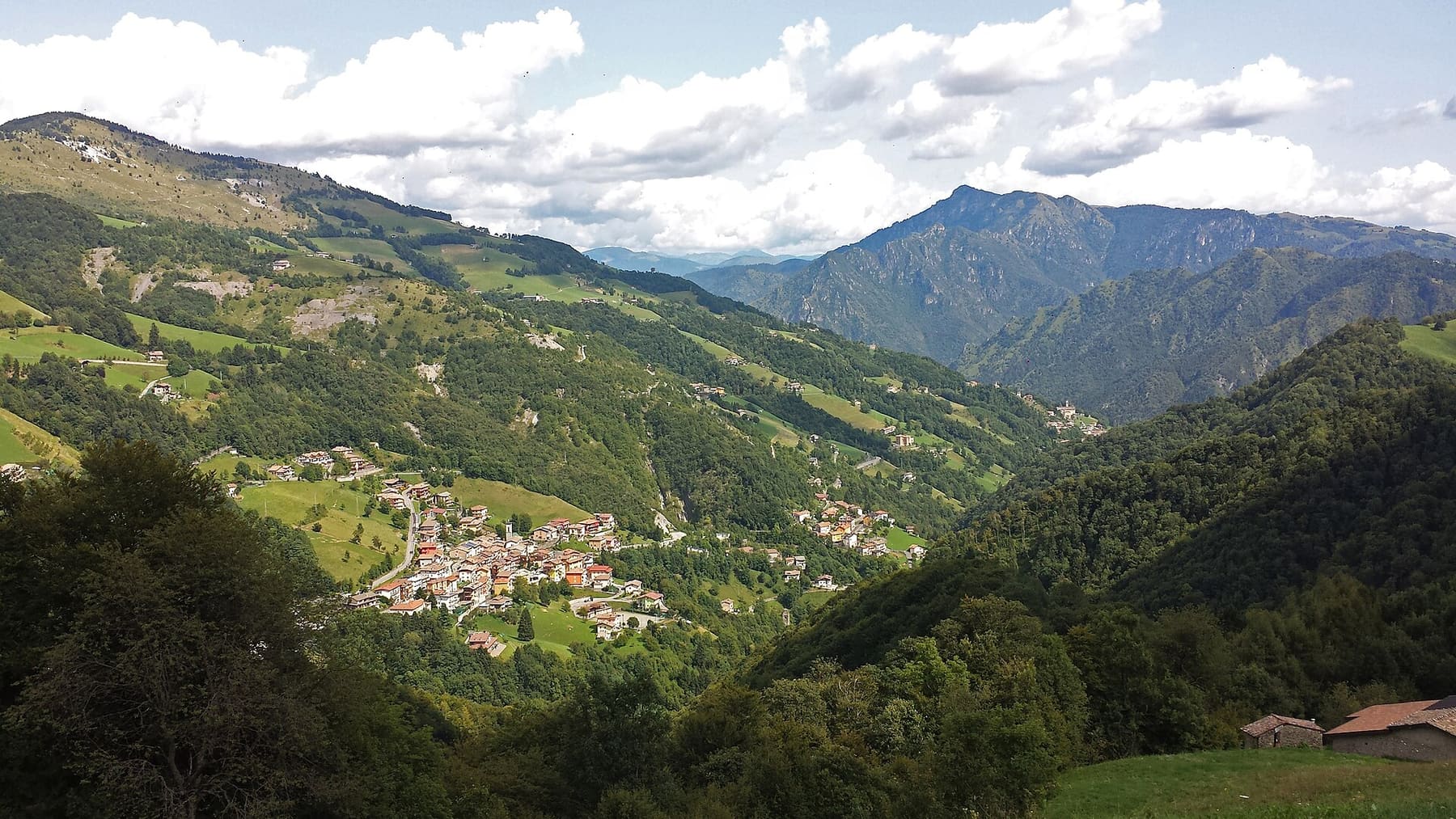 Il borgo di Oneta adagiato nella Val del Riso, con i prati e le cime della Val Seriana sullo sfondo