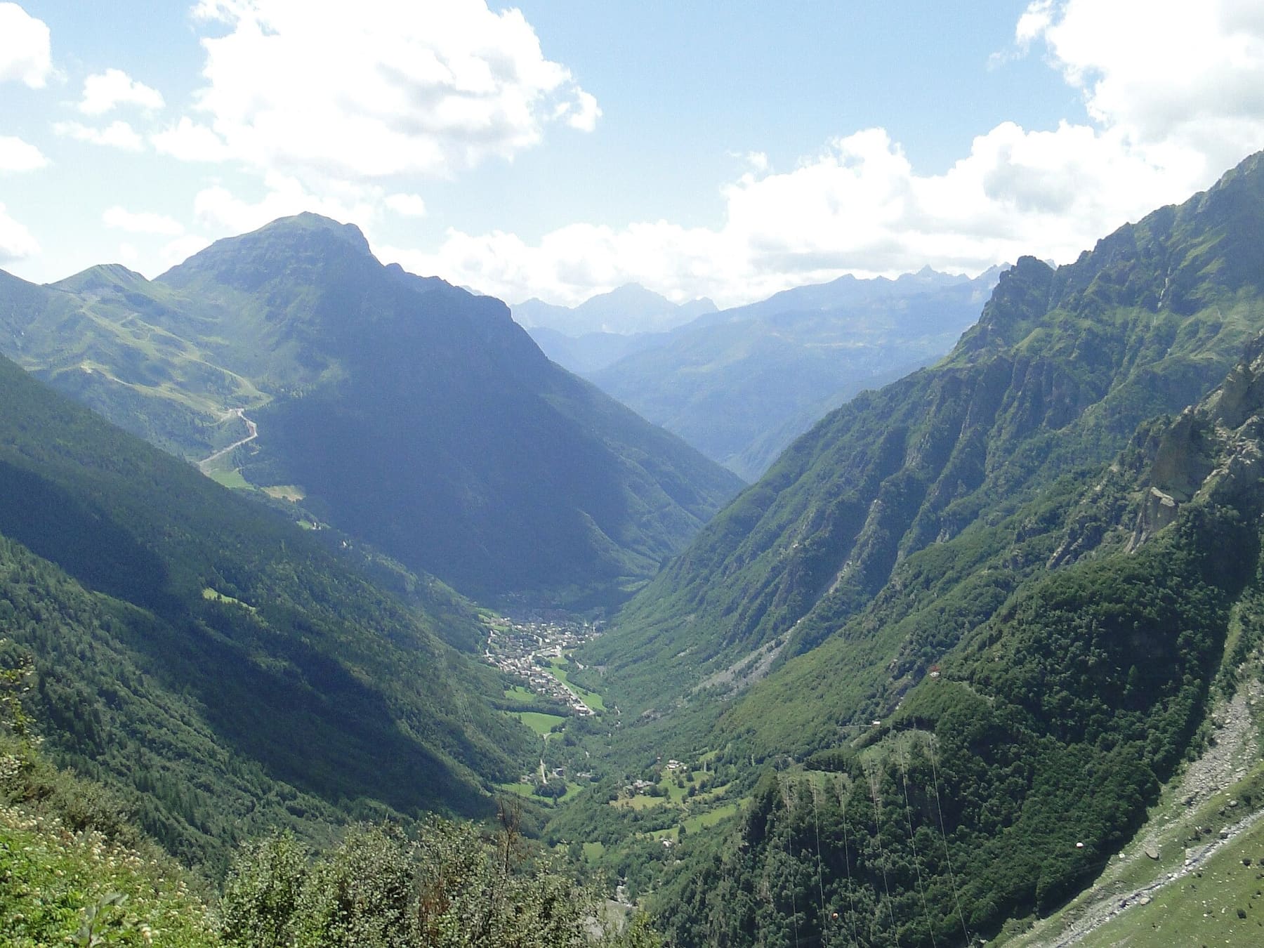 L'alta Valle Seriana vista dall'alto d'estate, con Valbondione nel fondovalle verde tra i versanti boscosi e le Orobie